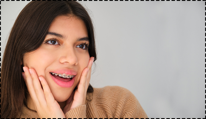 Woman smiling with hands on face, wearing tan sweater against neutral background