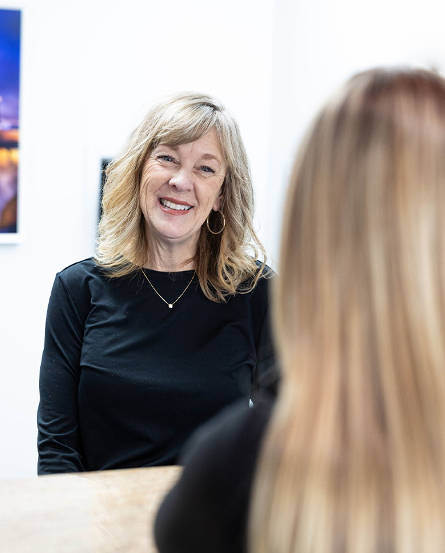 Woman with blonde hair smiling while conversing with patient in modern orthodontic office setting.