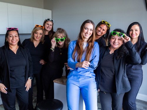 Team of eight women in professional attire posing together in a modern office setting.
